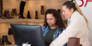 Foto de dos mujeres revisando una computadora en un negocio de calzado en Bogotá.