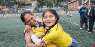 Imagen de una madre junto a su hija quien la abraza y sonríe