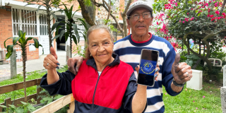 Imagen de dos personas mayores sonriendo y mostrando un celular con la imagen de Ingreso Mínimo Garantizado