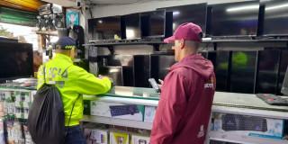 Policía y funcionario del Distrito inspeccionando establecimiento comercial dedicado a la compra y venta de equipos tecnológicos.