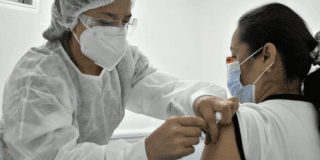 Imagen de una enfermera aplicando una vacuna a una mujer de mediana edad que usa tapabocas