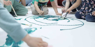 Foto que muestra niños y niñas con pintando en una cartulina con pinceles y pinturas 