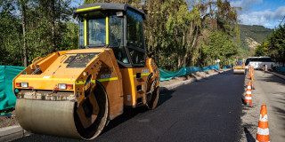Maquina amarilla en operación pavimenta vía urbana con señalización vial 