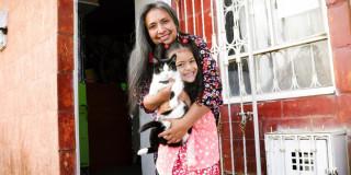 Imagen de una mujer abrazando a una niña que está cargando a un gato.