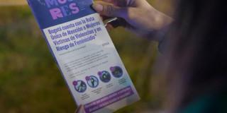 Mano sosteniendo folleto de la SDMujer en el que se lee: "Bogotá cuenta con la Ruta Única de Atención a Mujeres Víctimas de Violencias y en Riesgo de Feminicidio".