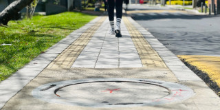 Foto que muestra una persona caminando por un andén en el que se ve una tapa de alcantarillado