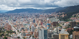 Panorámica de Bogotá con vista a viviendas, edificios, cerros orientales y cielo mayormente nublado.