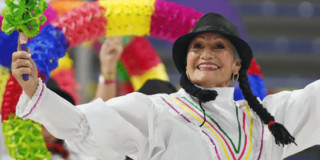 Persona mayor participa en actividad cultural con vestuario tradicional y accesorios coloridos durante presentación recreativa