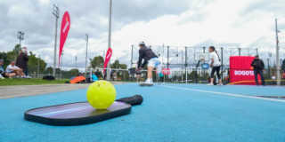 Raqueta de pickleball y una bola verde en un cancha para practicar este deporte
