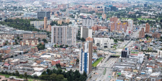 Vista aérea de Bogotá con edificaciones, avenidas principales y zonas verdes en día nublado.