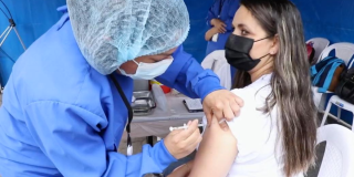 Imagen de una enfermera aplicando una vacuna a una mujer de mediana edad que usa tapabocas
