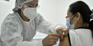 Imagen de una enfermera aplicando una vacuna a una mujer de mediana edad que usa tapabocas