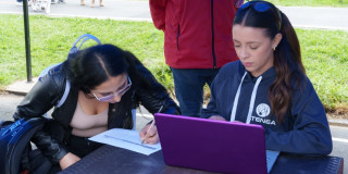 Foto que muestra dos mujeres sentadas escribiendo en un papel sobre una mesa