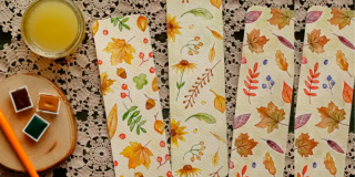 Imagen de una mesa en la que hay unas pinturas, un picnel y tres servilletas con dibujos de flores.