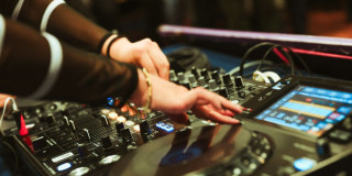 Imagen de consola de música eléctronica con manos de mujer tocando discos