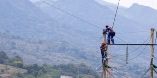 Imagen que muestra dos técnicos de Enel realizando mantenimiento a un poste de luz, de fondo se ve la ciudad.