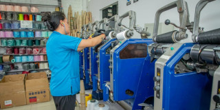Foto de una mujer trabajando junto a una maquina en una empresa de textiles en Bogotá.