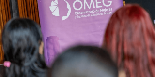 Mujeres con una pancarta del OMEG de fondo.