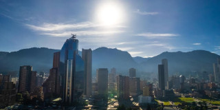 Vista panorámica de Bogotá con edificios modernos, cerros orientales y sol alto sobre cielo despejado