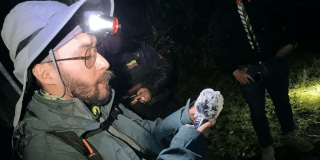 Participante observa una polilla durante jornada nocturna de monitoreo de biodiversidad en Bogotá, utilizando linterna frontal y equipos de registro en un área natural.