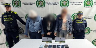 Tres mujeres capturadas en medio de dos policías. Los celulares recuperados están frente a ellas sobre una mesa.