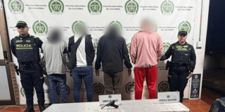 Cuatro capturados en medio de dos policías. El arma incautada está sobre una mesa.