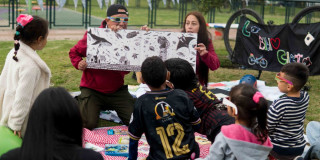 Imagen de dos personas mostranto un libro ilustrativo a niños en zona verde