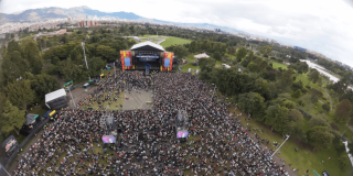 Vista aérea de concierto masivo en el parque Simón Bolívar con miles de asistentes reunidos frente a un escenario principal rodeado de zonas verdes y árboles.