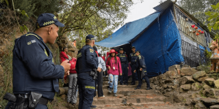 Policías y autoridades en sendero de Monserrate realizan operativo de sellamiento de estructura cubierta con lona azul y vegetación alrededor.