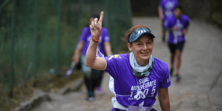 Imagen de referencia sobre participante de la carrera Sube Monserrate avanza por el sendero empedrado, viste camiseta morada con el texto “Sube Monserrate” y lleva el número de competencia sujeto a la cintura.