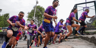 Imagen de referencia sobre participantes de la carrera Sube Monserrate ascienden al inicio del recorrido, vistiendo camisetas moradas del evento y números de competencia visibles en el pecho.