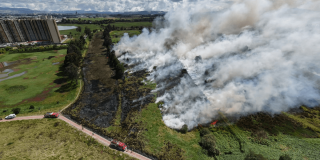 Vista aérea del humedal Jaboque durante un incendio de cobertura vegetal, con extensas columnas de humo, áreas afectadas por el fuego, vehículos de emergencia y edificaciones cercanas.