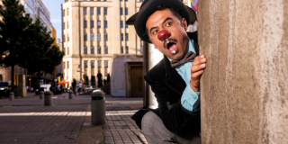 Imagen de Hombre con sombrero y nariz de payaso con corbatín asomándose por una columna de pared del Centro de Bogotá 
