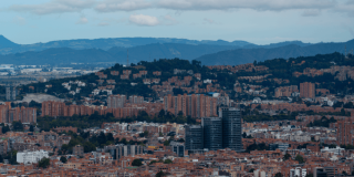 Vista panorámica de Bogotá con edificios residenciales y comerciales, centro financiero, cerros orientales y cielo parcialmente nublado.