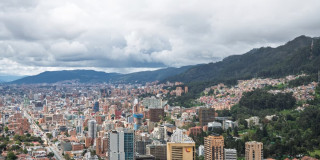 Vista panorámica de Bogotá con edificaciones densas, cerros orientales y cielo nublado amplio