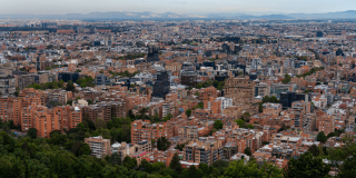 Vista panorámica de Bogotá con alta concentración de edificios residenciales y comerciales, amplias zonas arboladas en primer plano y expansión urbana que se extiende hacia el occidente de la ciudad.