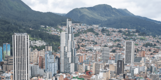 Vista panorámica del centro de Bogotá con edificios residenciales y empresariales de gran altura, cerros orientales cubiertos de vegetación y cielo nublado sobre la ciudad.