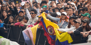 Asistentes a concierto en el parque Simón Bolívar permanecen frente a valla de seguridad del escenario, con banderas de Colombia visibles en primer plano.