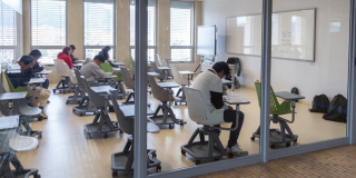 Foto que muestra estudiantes sentados en escritorios dentro de un salón 