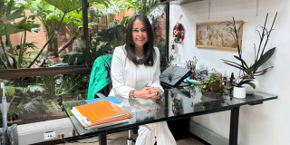 Tania Rodríguez dentro de una oficina rodeada de plantas ornamentales y vegetación visible a través de un ventanal en el Jardín Botánico de Bogotá. 