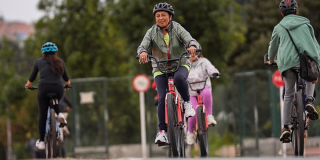 Personas recorren una ciclorruta en bicicleta durante una jornada recreativa rodeada de zonas verdes en Bogotá.