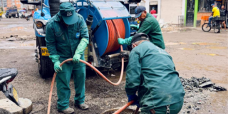 Imagen de tres técnicos de la empresa de Acueducto realizando mantenimiento en un tubo de alcantarillado, de fondo se ve un carro tanque.
