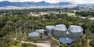 Vista panorámica del Jardín Botánico de Bogotá con Tropicario, zonas verdes y viviendas y edificaciones al fondo