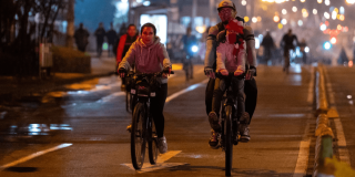 Personas recorren en bicicleta una vía iluminada de Bogotá durante una jornada de Ciclovía nocturna