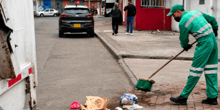 Foto que muestra una persona barriendo la calle y un camion recolector