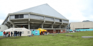Vista exterior del Palacio de los Deportes en Bogotá con carpas institucionales, personas y un punto de recepción de ayudas humanitarias instalado sobre una zona verde.