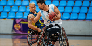 paradeportistas compiten en un partido de baloncesto en silla de ruedas dentro de un coliseo de Bogotá.