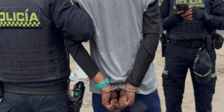 Hombre esposado, de espaldas, en medio de dos policías.