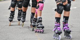 Primer plano de varias personas practicando patinaje sobre una vía, con patines en línea, cascos y elementos de protección.