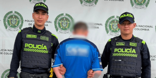 Hombre capturado, de espaldas, en medio de dos policías.